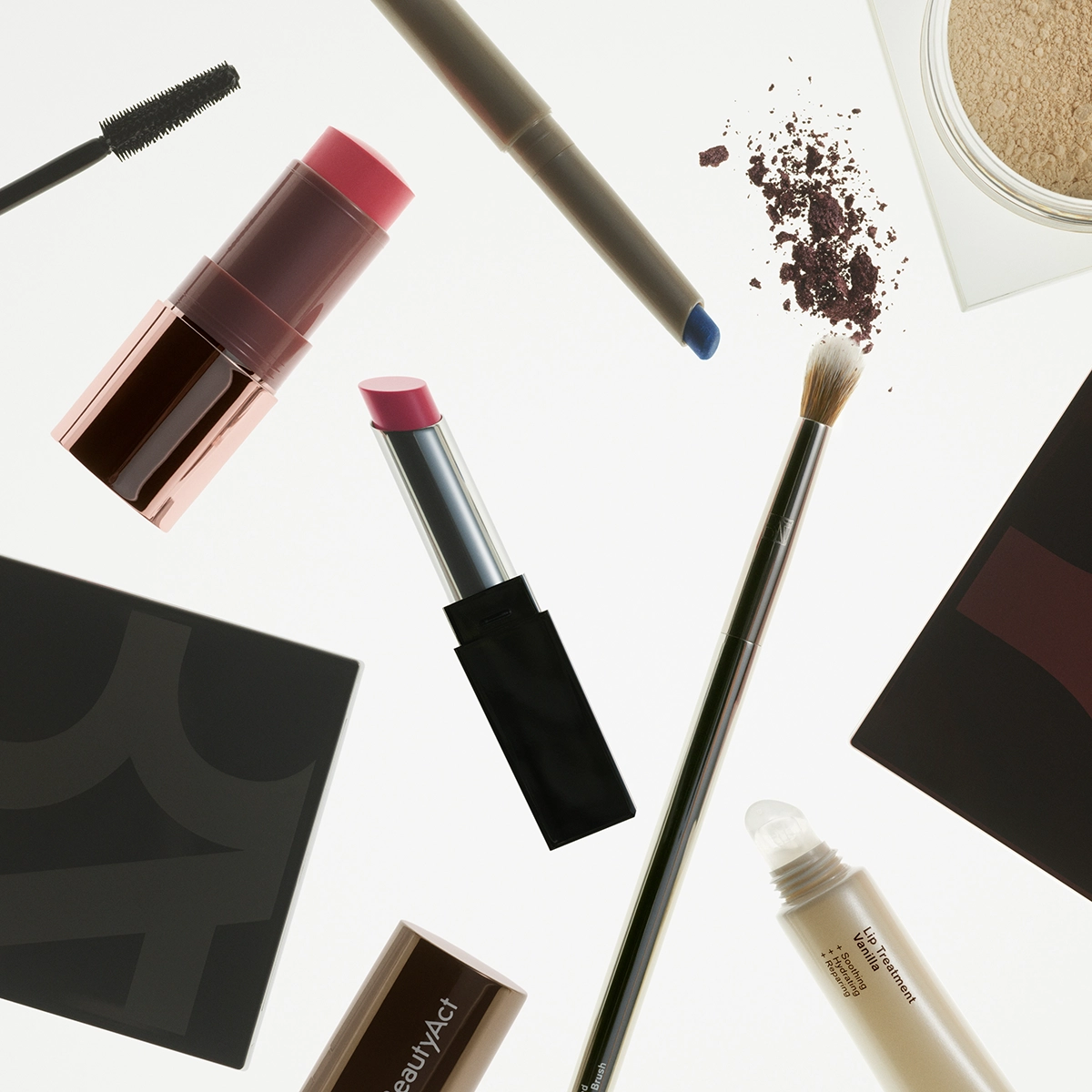 Makeupprodukter vises mot hvit bakgrunn, inkludert mascara, leppestift, øyenskygge, pudder, leppeblyant, leppebehandling og sminkekost sammen med makeup-paletter. Bildet inneholder produkter for makeup og skjønnhet med synlige detaljer som blå eyeliner, rosa leppeprodukter og løst pudder.