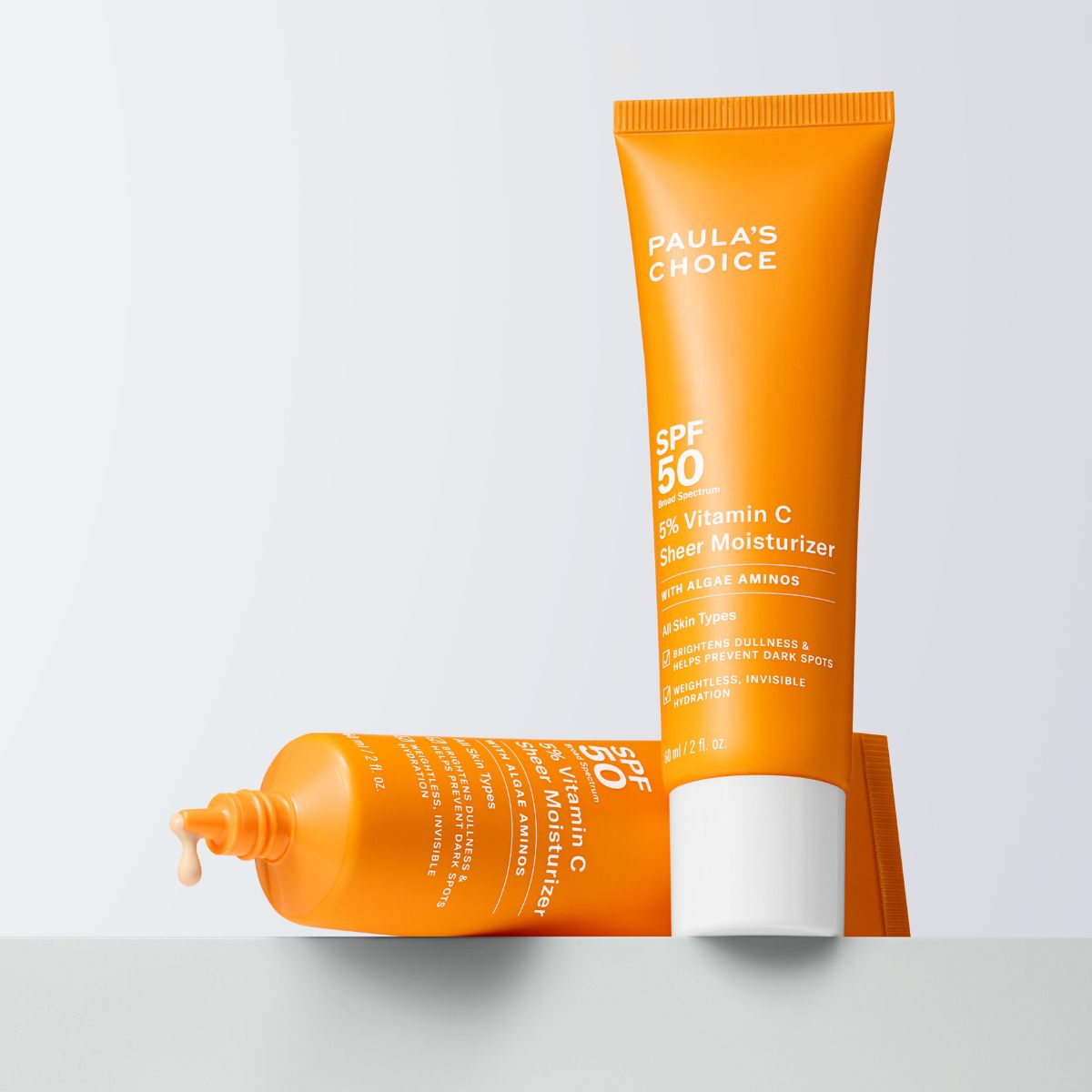 Paula's Choice - To oransje tuber med SPF 50 solbeskyttelse og 5% vitamin C. En tube ligger horisontalt og den andre står vertikalt.