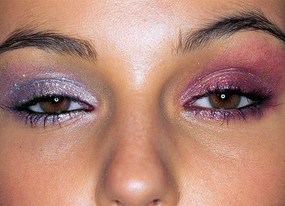 Brune øyne med uensartet skimrende øyenskygge - lilla på det ene øyelokket og rødrosa på det andre.