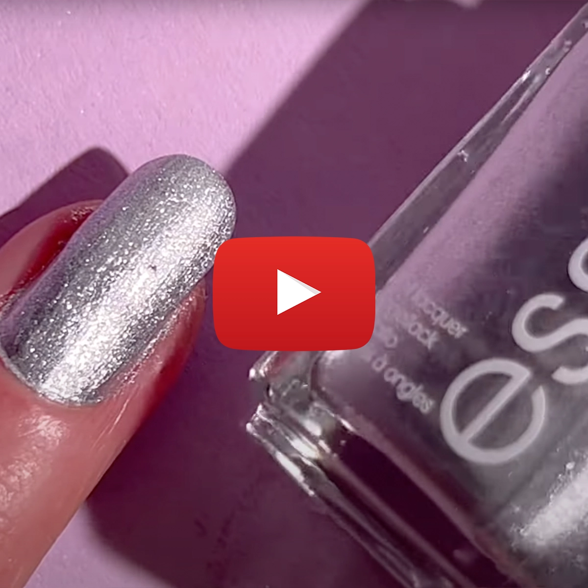 En närbild på en hand med silverfärgat nagellack och en flaska Essie nagellack. Ett Youtube play-tecken är placerat i mitten av bilden.