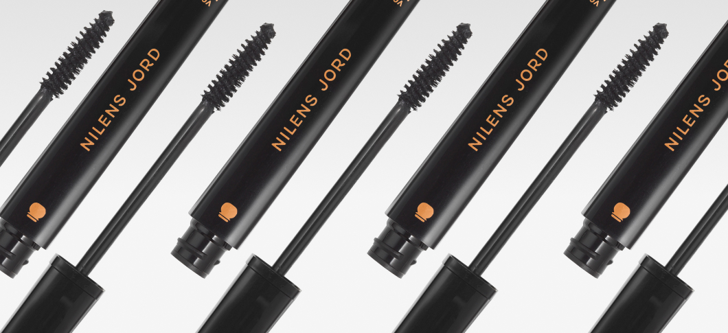 Flera svarta Nilens Jord-mascaror med öppna borstar är arrangerade diagonalt mot ljus bakgrund, med produktnamnet i kopparfärgad text.