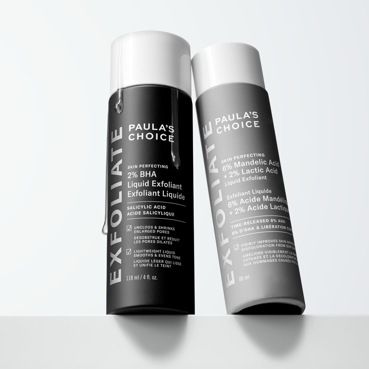 Paula's Choice - To hudpleieprodukter står på en hvit overflate. En svart flaske og en grå flaske, begge med hvite korker.