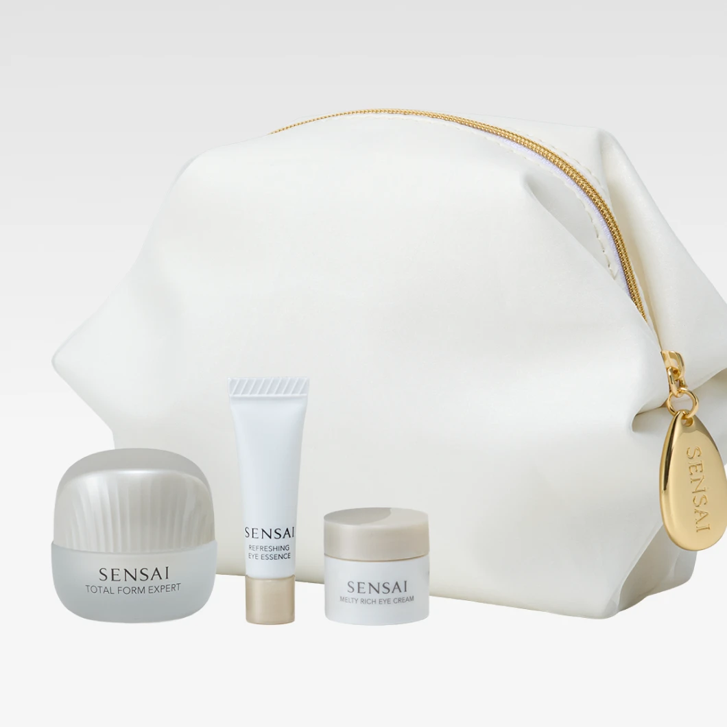 Valkoinen Sensai-kosmetiikkalaukku kullanvärisellä vetoketjulla sekä Sensai Total Form Expert, Refreshing Eye Essence ja Melty Rich Eye Cream vaalealla taustalla. “SENSAI” näkyy tuotteissa ja vetoketjun kullanvärisessä riipuksessa.