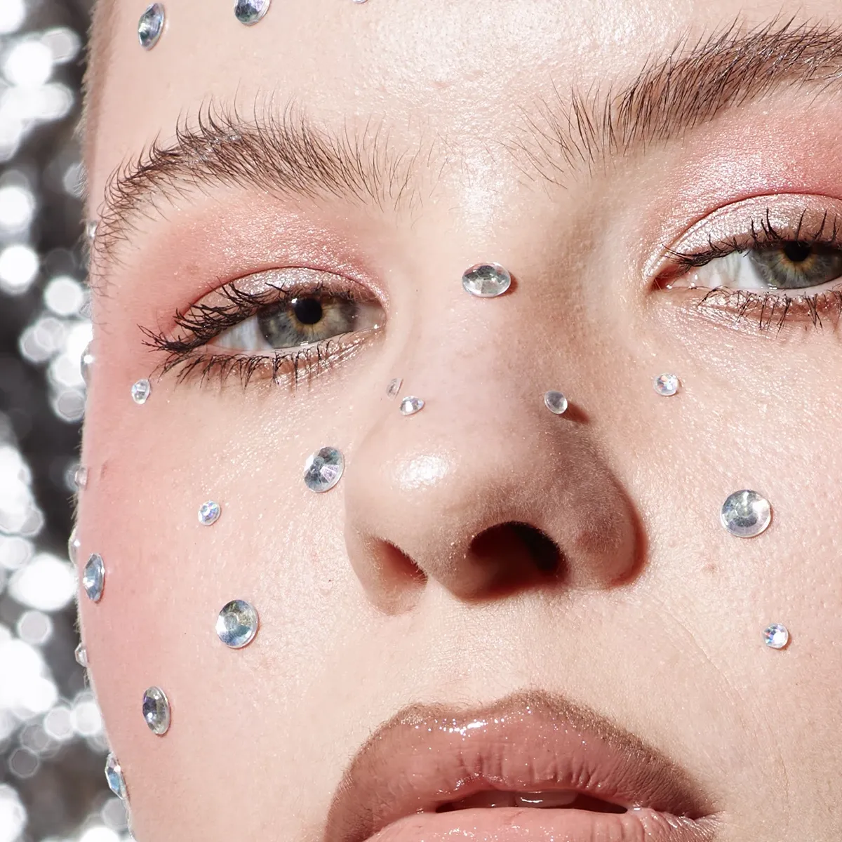 Kvinne med naturlig sminke, maskara og rhinestones rundt ansiktet som fregner.
