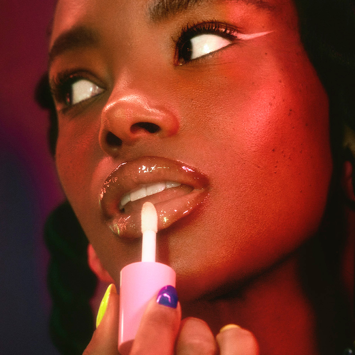 Tummahiuksinen nainen levittää tuotetta huulille vaaleanpunaisella applikaattorilla.