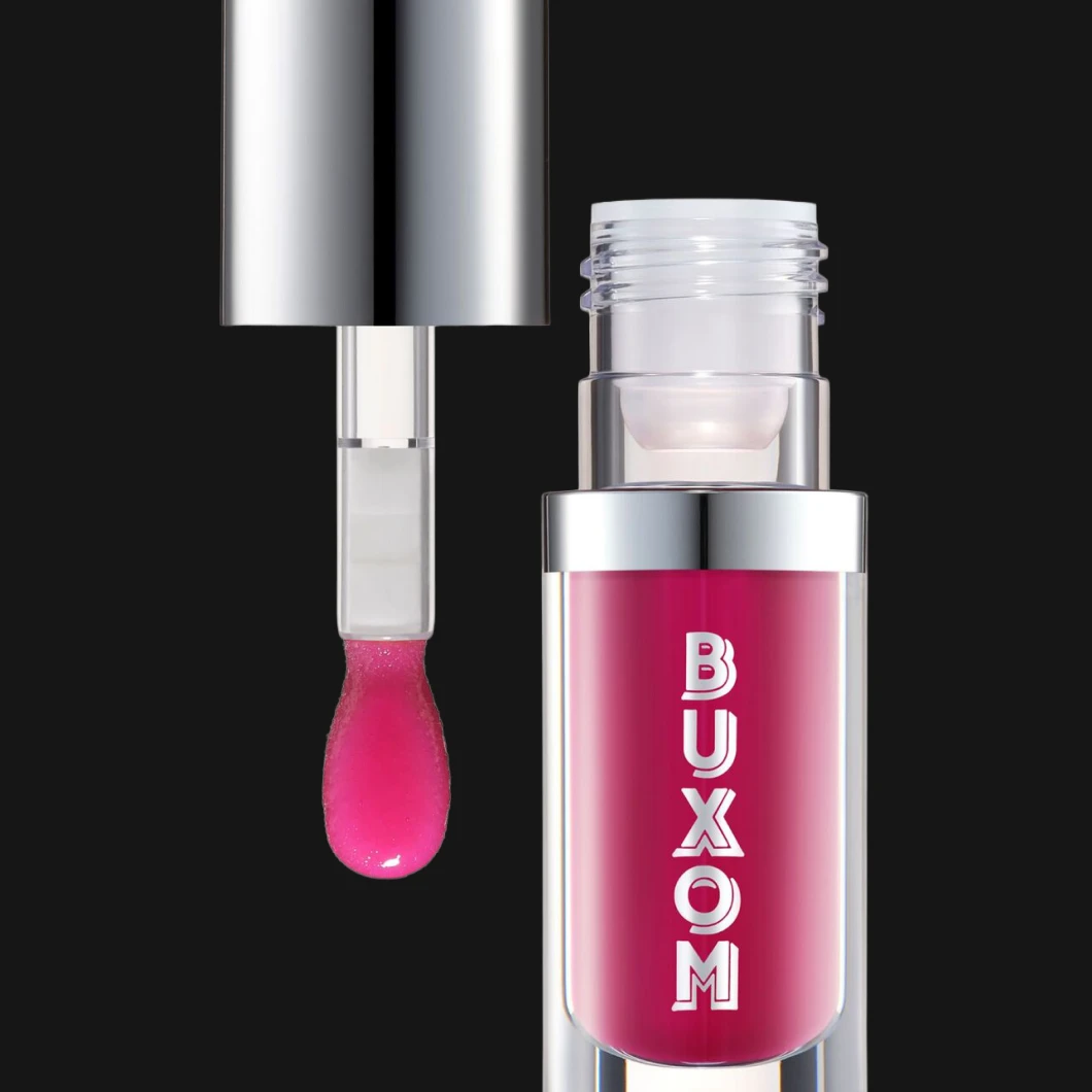 Rosa lipgloss i gjennomsiktig flaske med teksten BUXOM, åpnet med applikator over flasken mot svart bakgrunn.
