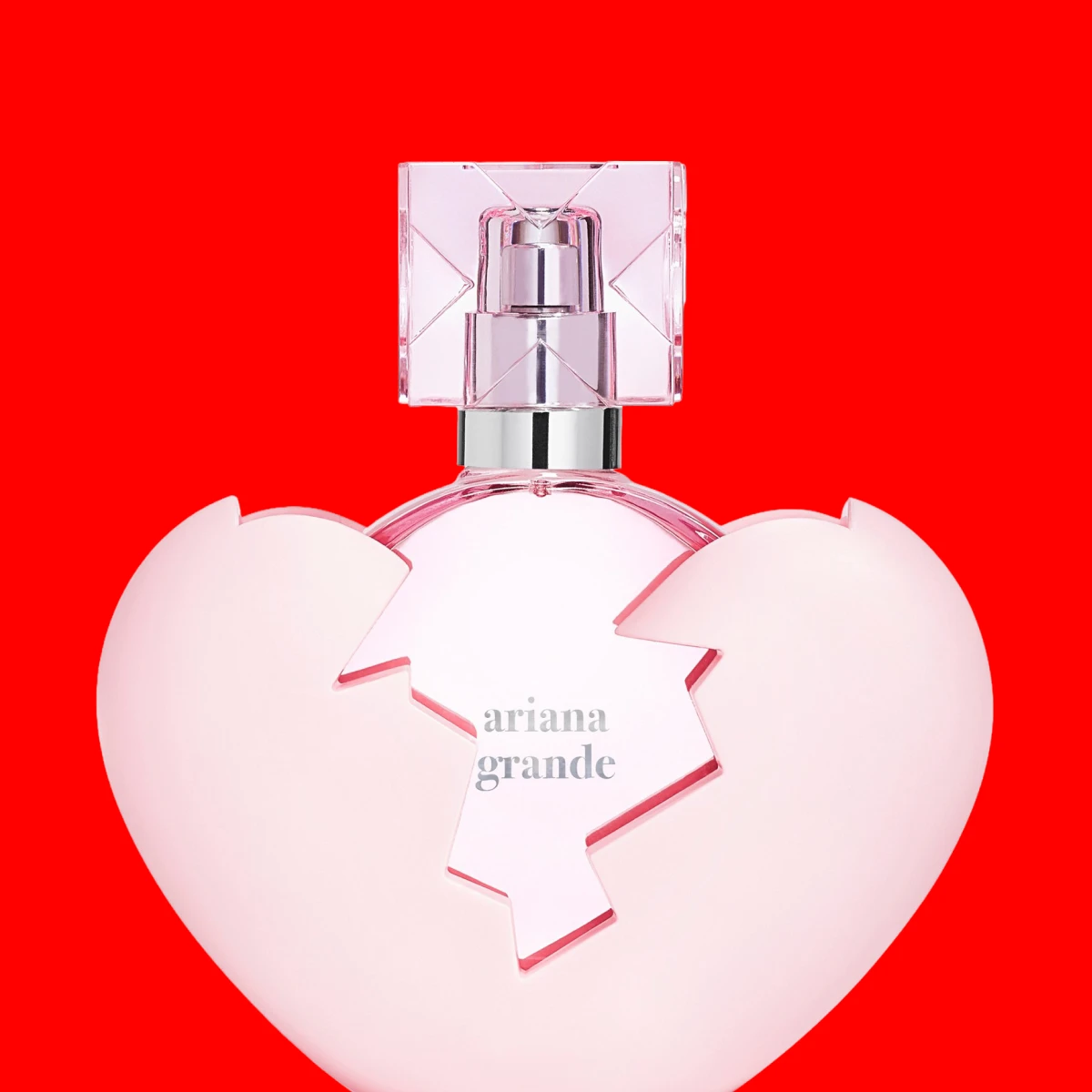Rosa, hjerteformet parfymeflaske med gjennomsiktig midtseksjon mot rød bakgrunn