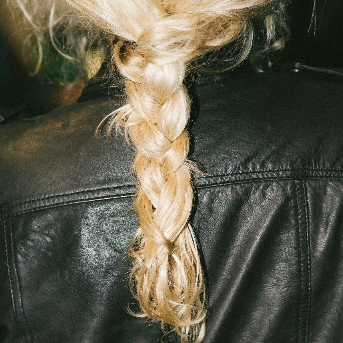 Nærbilde av en flette i lyst blondt hår over en svart skinnjakke, med fokus på hårstruktur og styling for hårpleie.