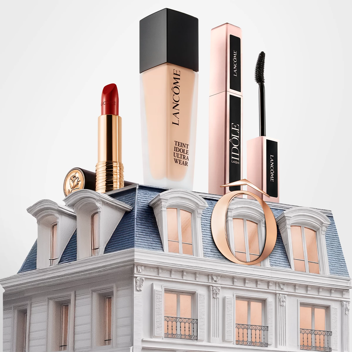 Fyra Lancôme sminkprodukter, inklusive en röd läppstift, foundation, mascara och eyeliner, placerade på taket av en elegant byggnad med blått tak och fönster.