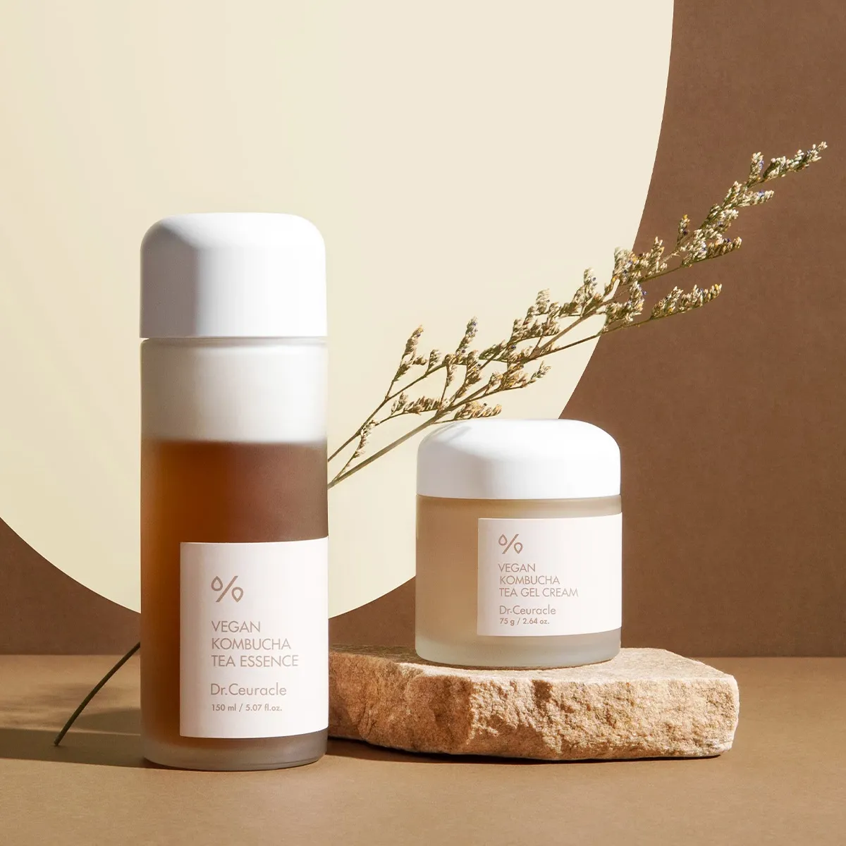 To hudpleieprodukter fra Dr.Ceuracle står plassert mot en beige og brun bakgrunn med en dekorativ plante.