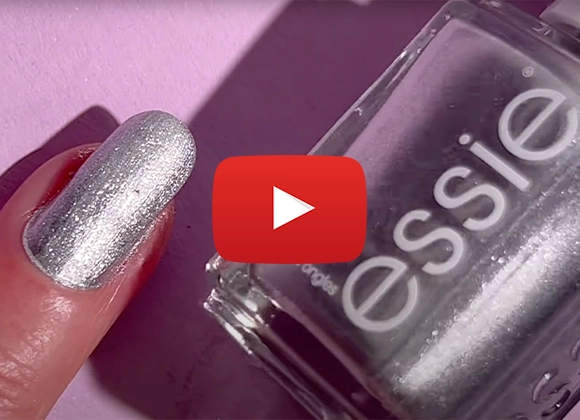 En närbild på en hand med silverfärgat nagellack och en flaska Essie nagellack. Ett Youtube play-tecken är placerat i mitten av bilden.