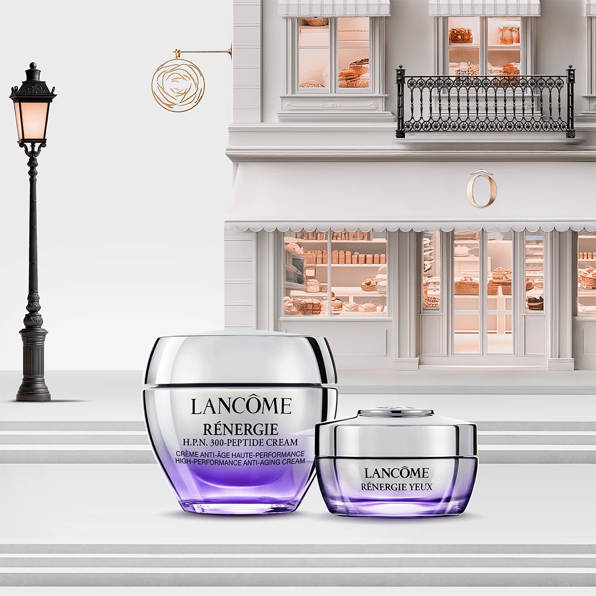 Två Lancôme Rénergie hudvårdsprodukter med lila och silverfärgad förpackning framför en elegant byggnad med balkong och butiksvinduer. En lyktstolpe står till vänster.