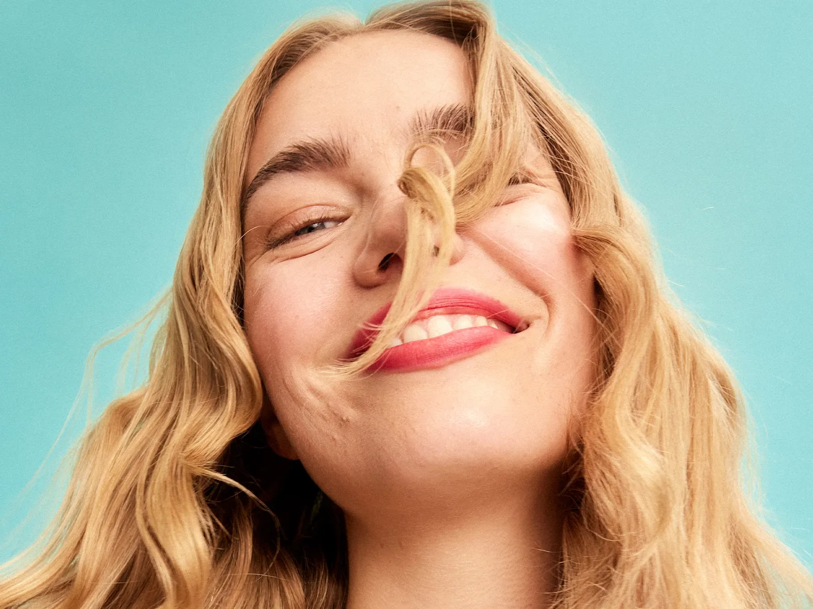 En person med långt blont hår mot en blå bakgrund. Ansiktet är suddat.