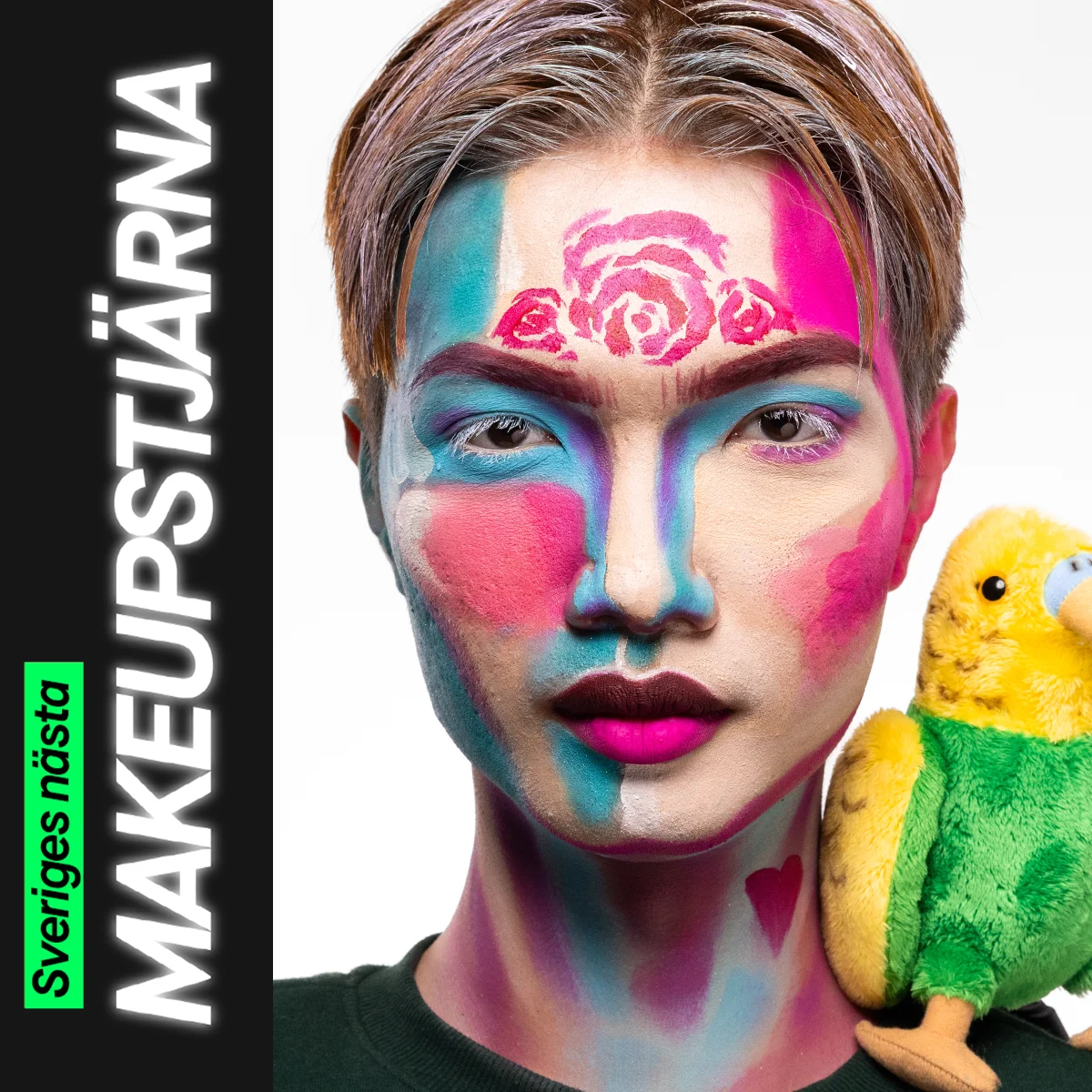 En person med färgstark ansiktsmålning i blå, rosa och lila blockfärger tillsammans med målade rosor i pannan och neonrosa läppar, poserar bredvid en grön och gul gosedjursfågel.
