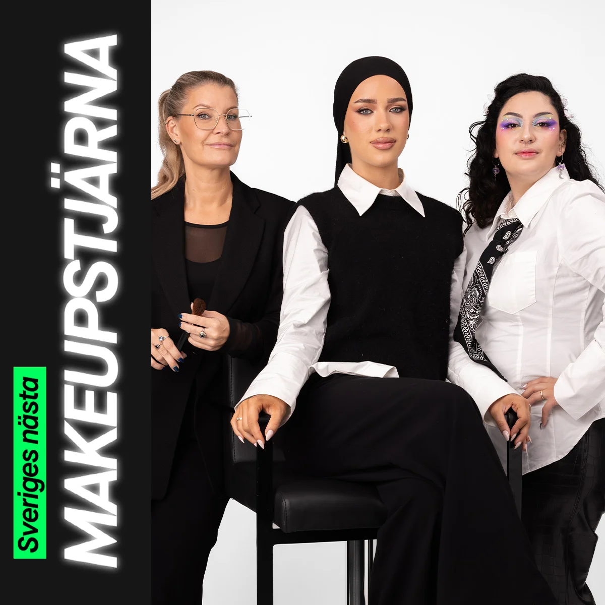 Tre personer sitter tillsammans, där en håller en makeupborste och de andra bär kreativa makeuplooker – en med markerad bas och eyeliner samt en med färgstark ögonmakeup med glitterdetaljer.