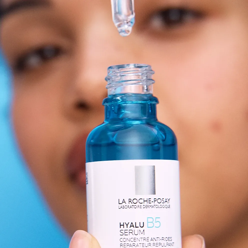 En kvinna visar upp ett serum från La Roche-Posay mot en blå bakgrund.
