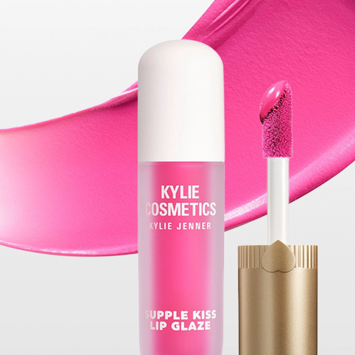 Kylie Cosmetics Supplе Kiss Lip Glaze lipgloss i rosa nyanse med applikator og utsmurt gloss-tekstur i bakgrunnen. Emballasjen viser teksten "KYLIE COSMETICS KYLIE JENNER SUPPLE KISS LIP GLAZE".