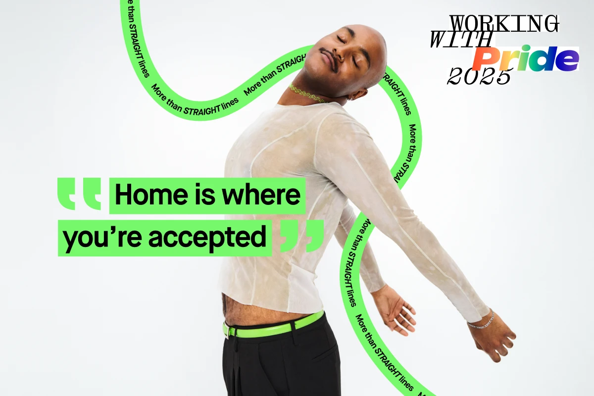 Henkilö poseeraa valkoisessa pitkähihaisessa paidassa ja mustissa housuissa, joissa on vihreä vyö, valkoista taustaa vasten. Kuvassa on teksti "Home is where you’re accepted" ja taustalla on kaarevia viivoja tekstillä "More than STRAIGHT lines". Oikeassa yläkulmassa lukee "WORKING WITH Pride 2025".