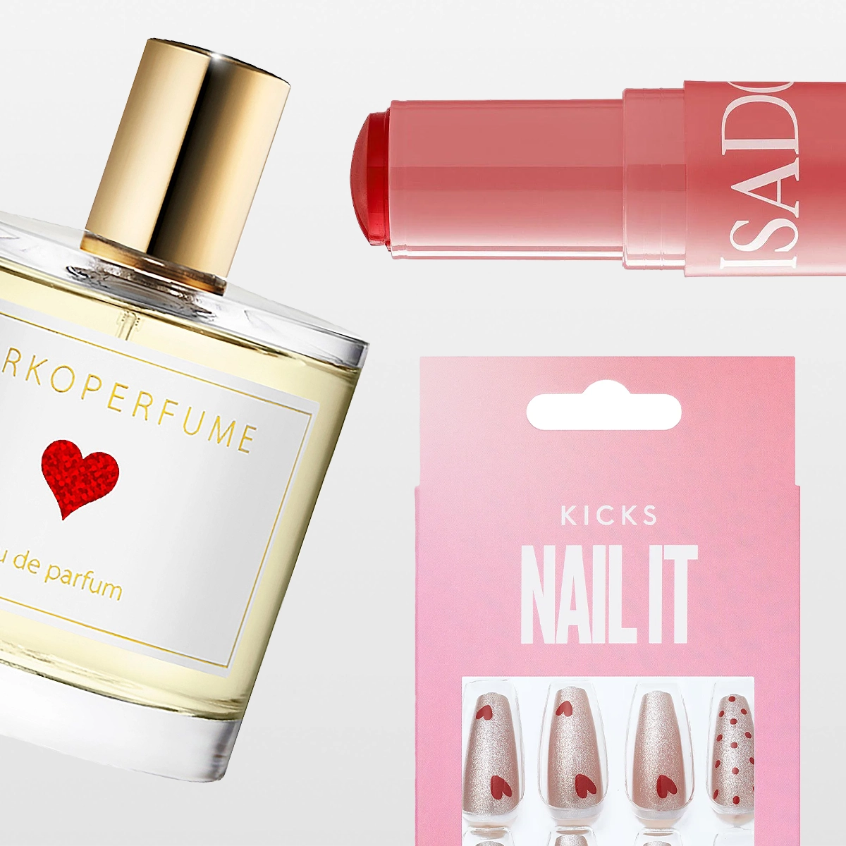 Ett urval skönhetsprodukter mot ljus bakgrund. En parfymflaska med guldfärgad kork och etikett med rött hjärta, ett rosa läppstift med texten “ISAD”, ett rosa förpackningskort märkt “KICKS NAILIT” samt lösnaglar i ljusrosa nyanser med hjärt- och prickmönster.