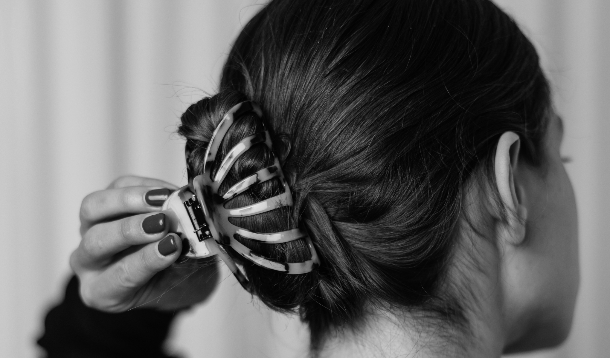 En person med brunt hår bruker en hårklype for å holde håret oppe. Klypen er svart og hvit og ser ut til å være laget av plast.