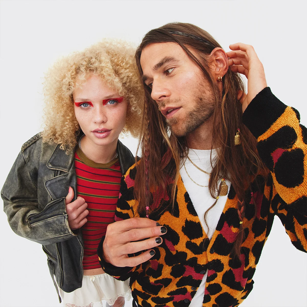 To personer poserer sammen, én med krøllete blondt hår og fargerik øyesminke og én med langt brunt hår og leopardmønstret cardigan.