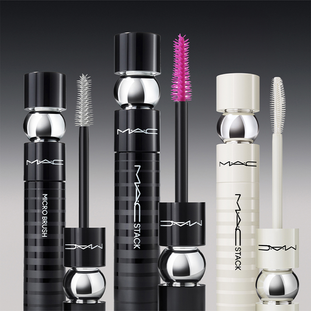 Fyra olika mascaror från MAC Cosmetics står uppradade mot en mörkgrå bakgrund. Förpackningarna är svarta och vita med silverdetaljer och MAC-logotypen syns tydligt på varje mascara. Borstarna är i olika färger.