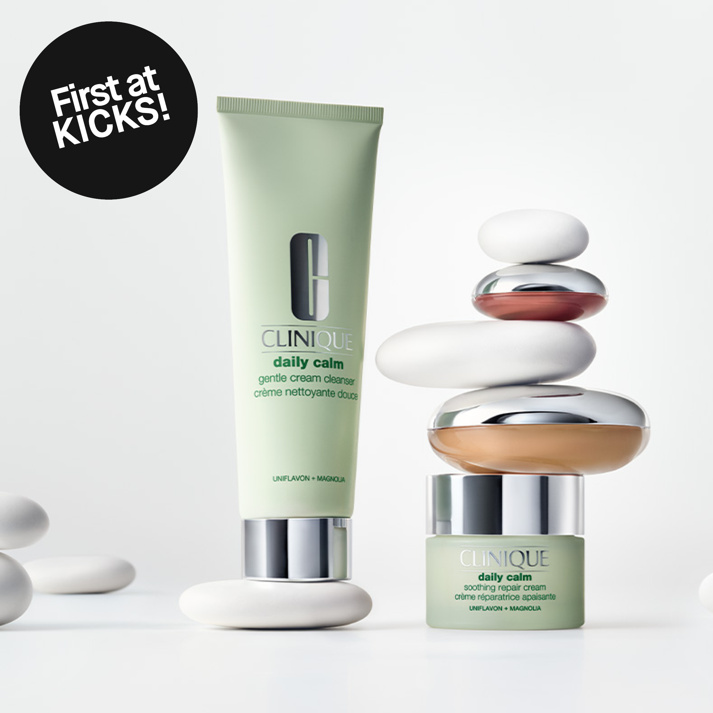Clinique Daily Calm-rens og ansiktskrem mot lys bakgrunn ved siden av balanserte steiner. Bildet inneholder teksten «First at KICKS!».