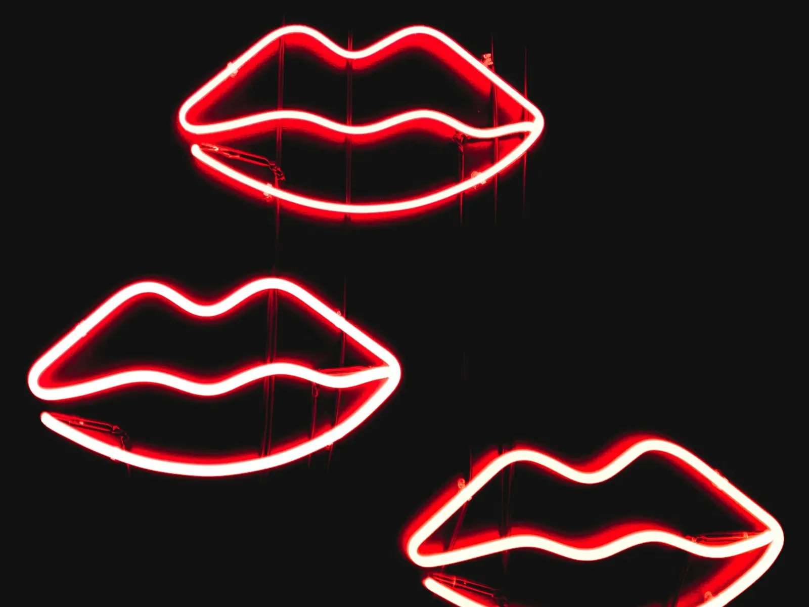 Tre røde neonlys i form av lepper mot en svart bakgrunn.