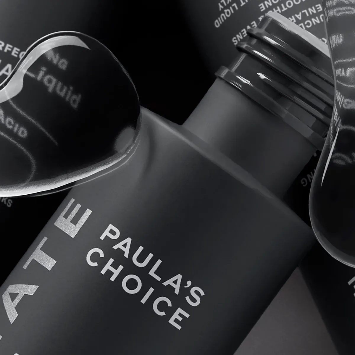 Tre produkter fra Paula's Choice i nærbilde med grå bakgrunn og vanndråper i forgrunnen.