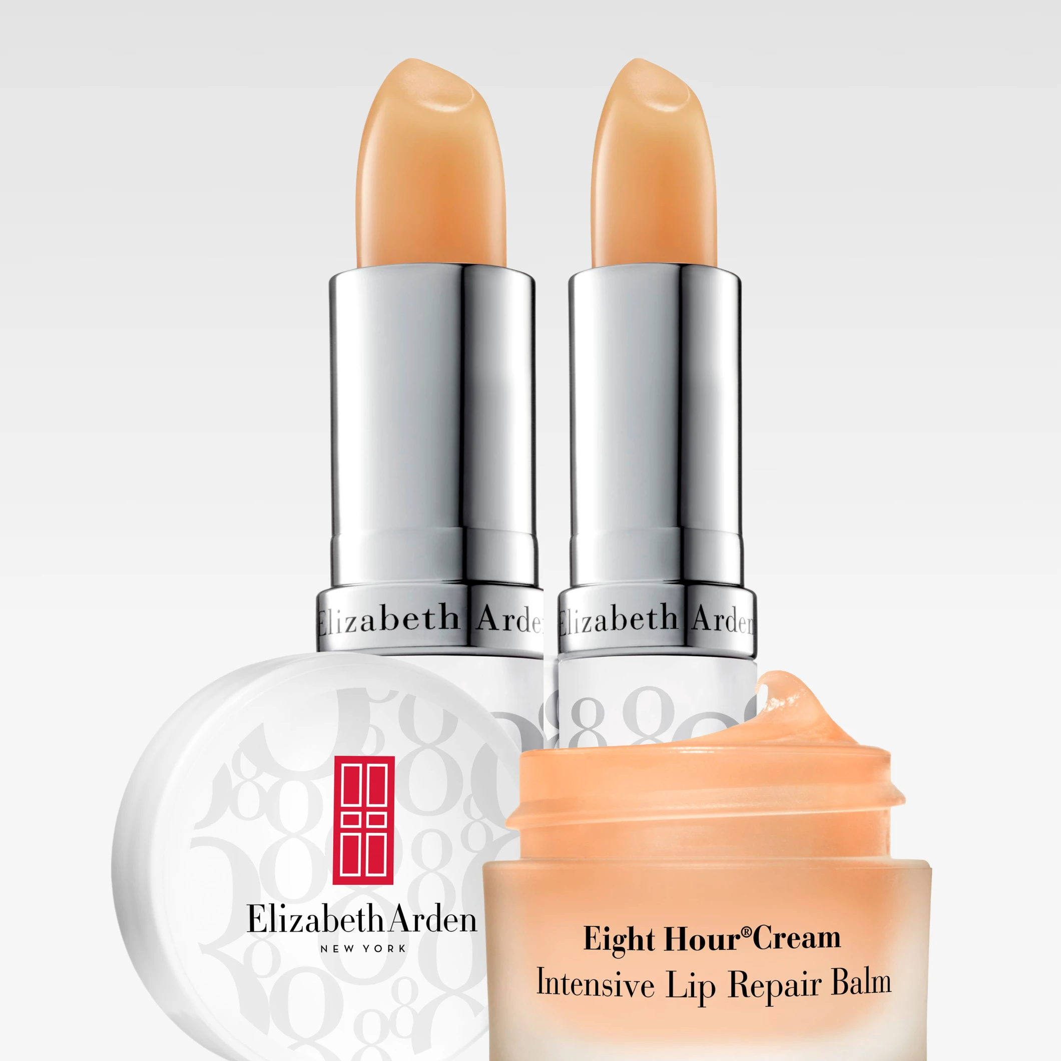 Produktbild med Elizabeth Arden Eight Hour-produkter. Två läppbalsamstift i silverfärgade hylsor, en öppen burk Eight Hour Intensive Lip Repair Balm med synlig kräm samt ett runt vitt lock med Elizabeth Arden-logotyp.