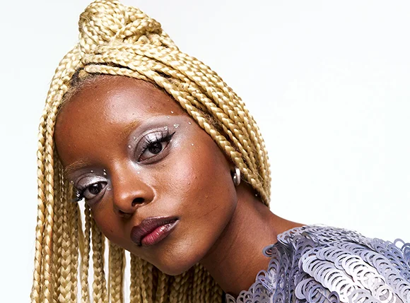 Modell med lange blonde fletter, metallisk øyenskygge og grafisk eyeliner – en inspirerende festlook med fokus på glød, trendy makeup og kreative beauty hacks