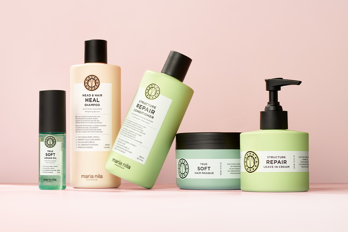 En samling hårvårdsprodukter från Maria Nila placerade mot en ljusrosa bakgrund. Flaskorna och burkarna har en stilren design med etiketter i olika färger.