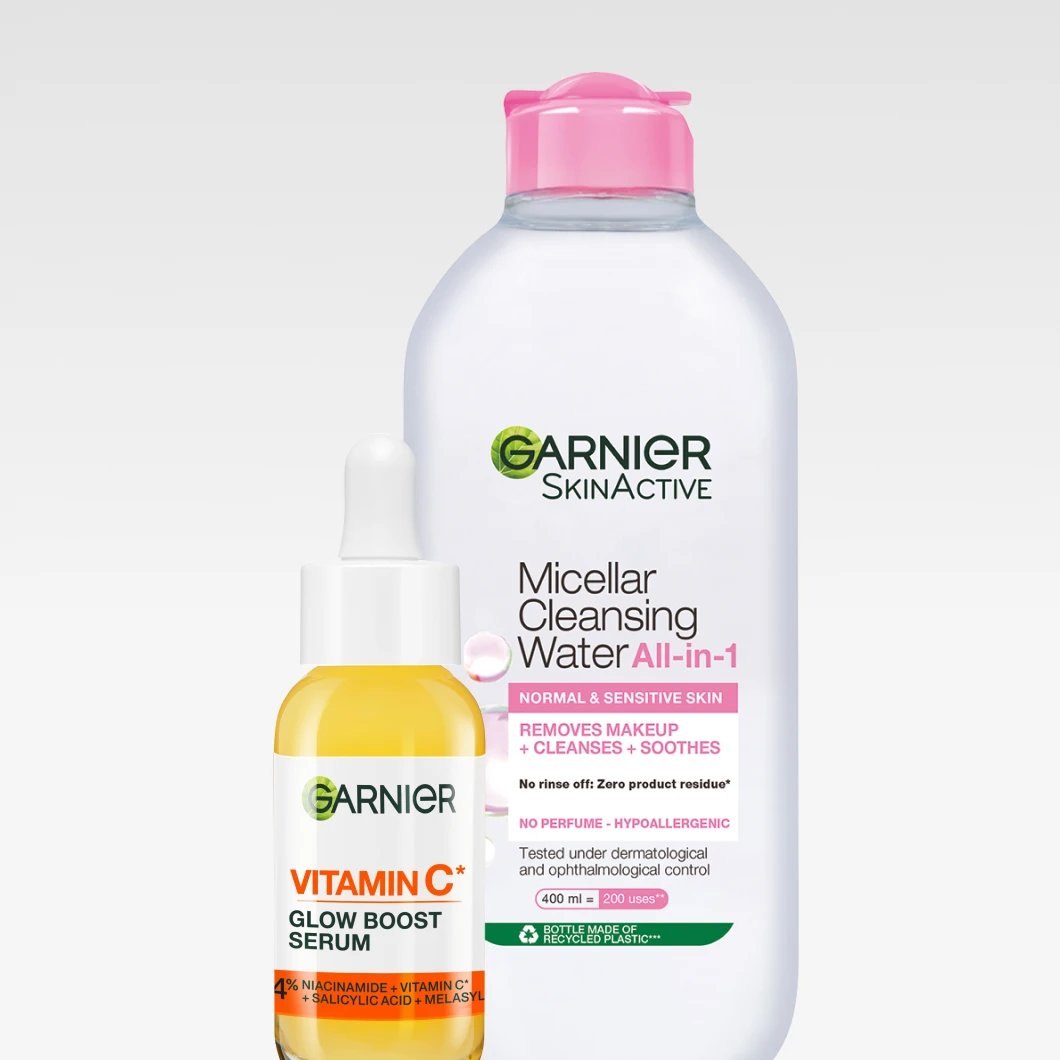 Nærbilde av to Garnier SkinActive-produkter mot en lys bakgrunn: en stor flaske Garnier Micellar Cleansing Water All-in-1 med rosa kork står bak en mindre glassflaske Garnier Vitamin C Glow Boost Serum med gul formel og pipette. Et rent og friskt uttrykk som fremhever hudpleiens glød.