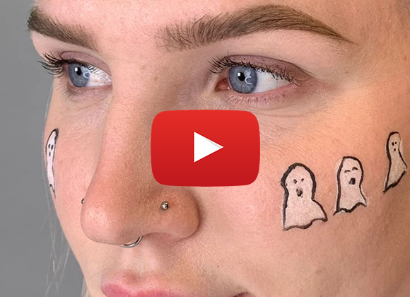 Nærbilde av en person som har tre hvite spøkelser tegnet på kinnet. Personen har en piercing i nesen. Det er en YouTube-play-symbol i midten av bildet.