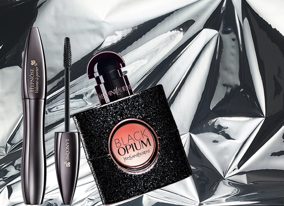 Lancôme Hypnôse Volume-maskara og Yves Saint Laurent Black Opium-parfyme er plassert mot en blank sølvbakgrunn som fremhever en glamorøs beautystemning.
