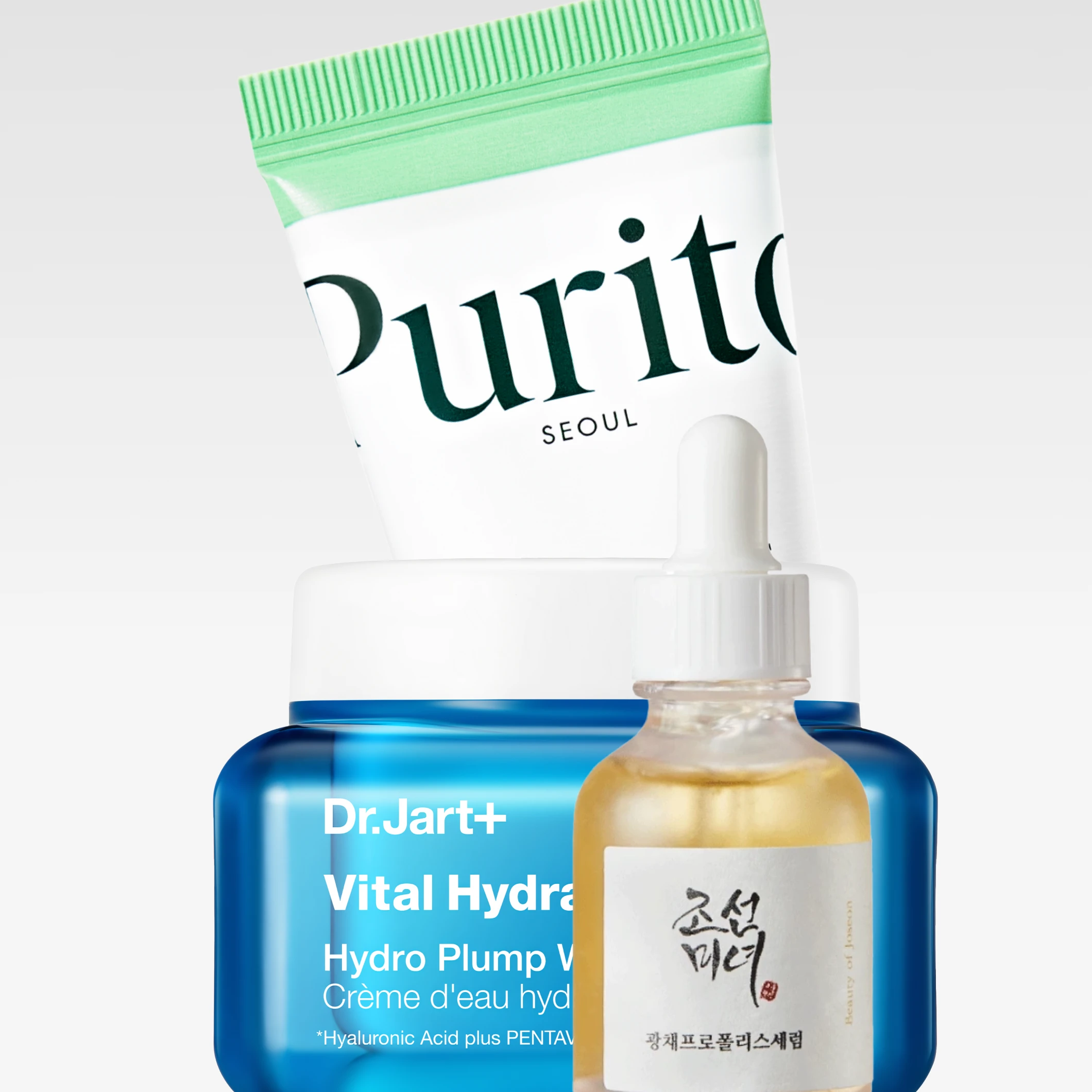 K-beauty-tuotteita vaaleanharmaata taustaa vasten: Purito Seoul -tuote, Dr.Jart+ Vital Hydra Solution Hydro Plump Water Cream sekä Beauty of Joseon -seerumi. Pakkauksissa näkyvät muun muassa tekstit ”Purito SEOUL”, ”Dr.Jart+”, ”Vital Hydra Solution”, ”Hydro Plump Water Cream” ja ”Beauty of Joseon”.