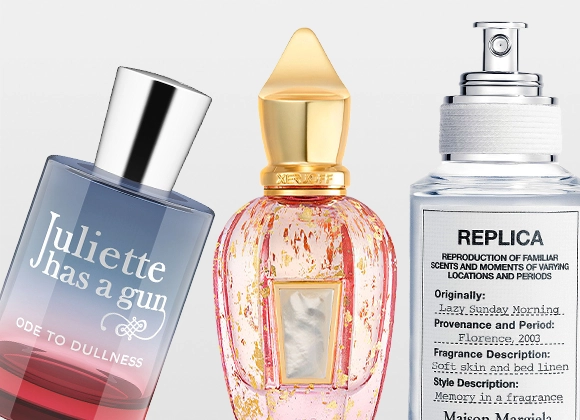 Produktbild med tre parfymflaskor mot ljus bakgrund. Till vänster syns en blå och rödtonad glasflaska märkt “Juliette has a gun – Ode to Dullness”. I mitten syns en rosa och guldfärgad parfymflaska med dekorativ kork. Till höger syns en klar glasflaska med vit etikett märkt “Replica” och texten “Maison Margiela”.