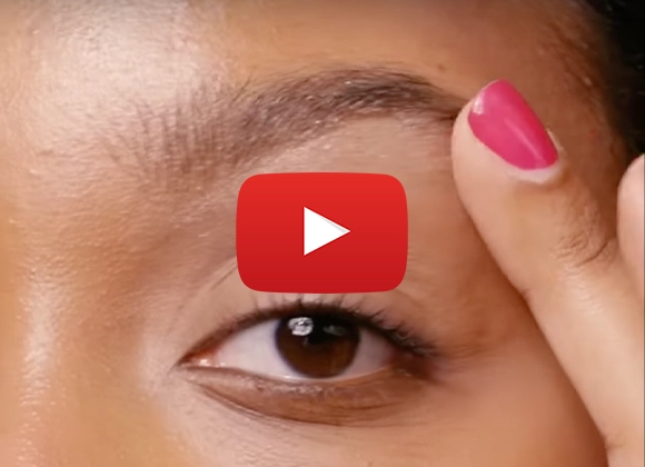 En närbild på en person som applicerar smink på ögonbrynet med en rosa nagel. Ett Youtube play-tecken är placerat i mitten av bilden.