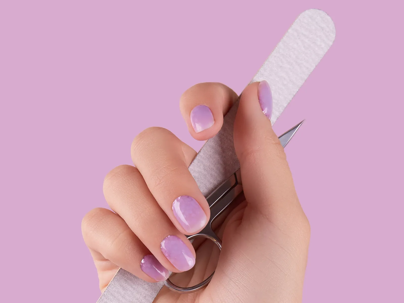 Käsi, joka pitää kynsiviilaa ja kynsisaksia. Kynnet ovat violetit ja tausta on violetti.