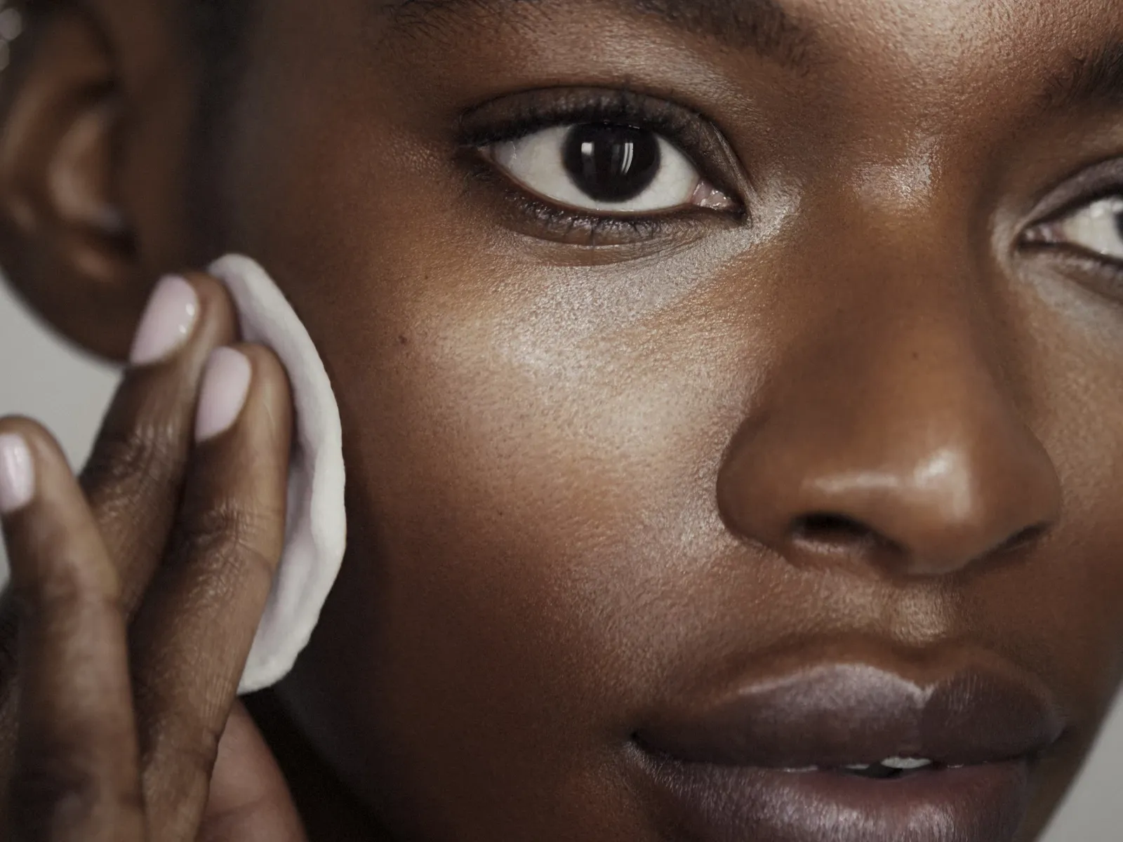 Henkilö, jolla on melaniinirikas ihonsävy, pyyhkii kasvojaan puuvillatyynyllä.