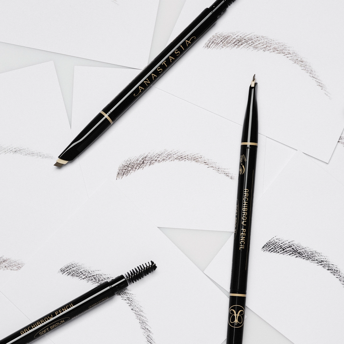 Svart øyenbrynsblyant fra Anastasia Beverly Hills med teksten "ANASTASIA" og "BROW WIZ", sammen med en spooliebørste og flere strøk av brynfarge på hvit bakgrunn.