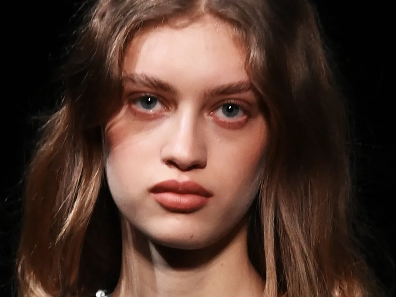 En person med langt, brunt hår står foran en svart bakgrunn.