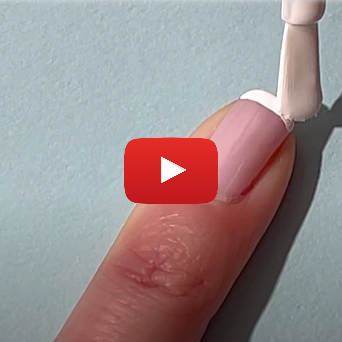 En närbild på en person som applicerar vitt nagellack på en ljusrosa nagel. Ett Youtube play-tecken är placerat i mitten av bilden.