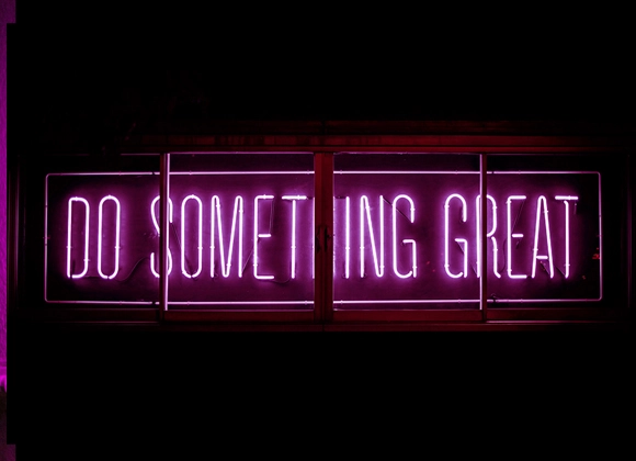 Rosa neonskilt med teksten "Gjør noe flott" mot en mørk bakgrunn.