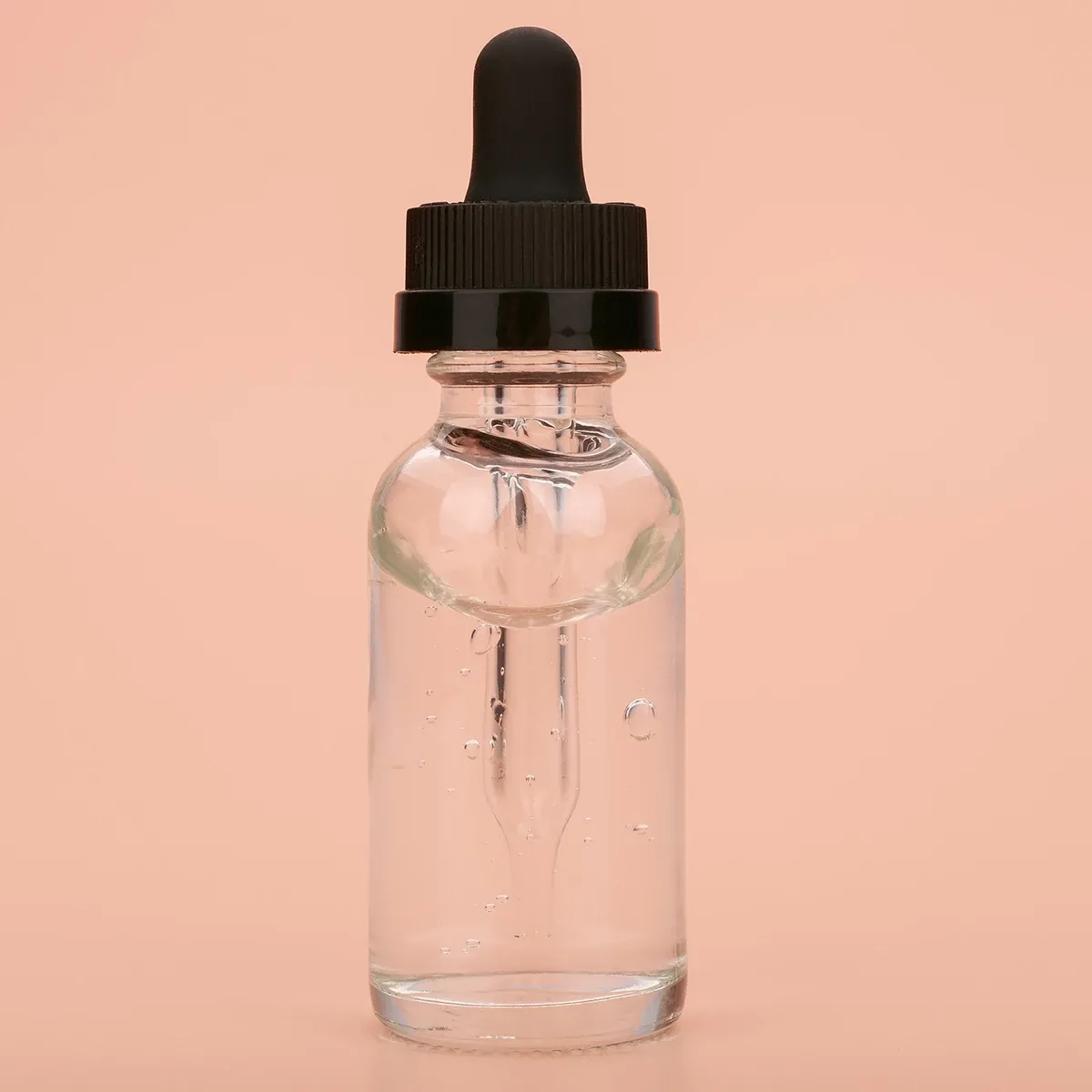 Gjennomsiktig pipetteflaske med hudpleieserum mot beige bakgrunn