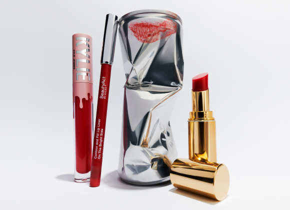 Røde leppeprodukter inkludert leppestift, lipgloss og leppeblyant, ved siden av en knust boks med et leppeavtrykk.