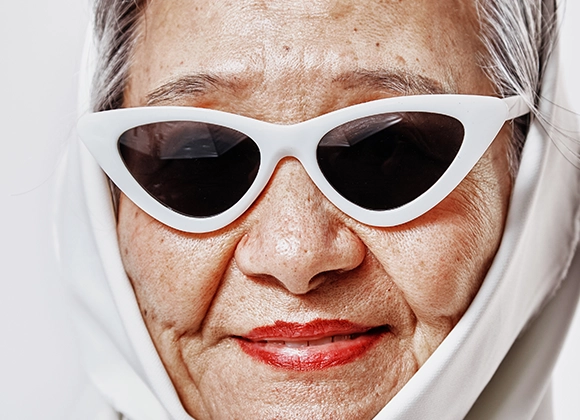 Närbild av en person som bär vita solglasögon och rött läppstift, med fokus på hud och läppar i en minimalistisk, ljus bakgrund.