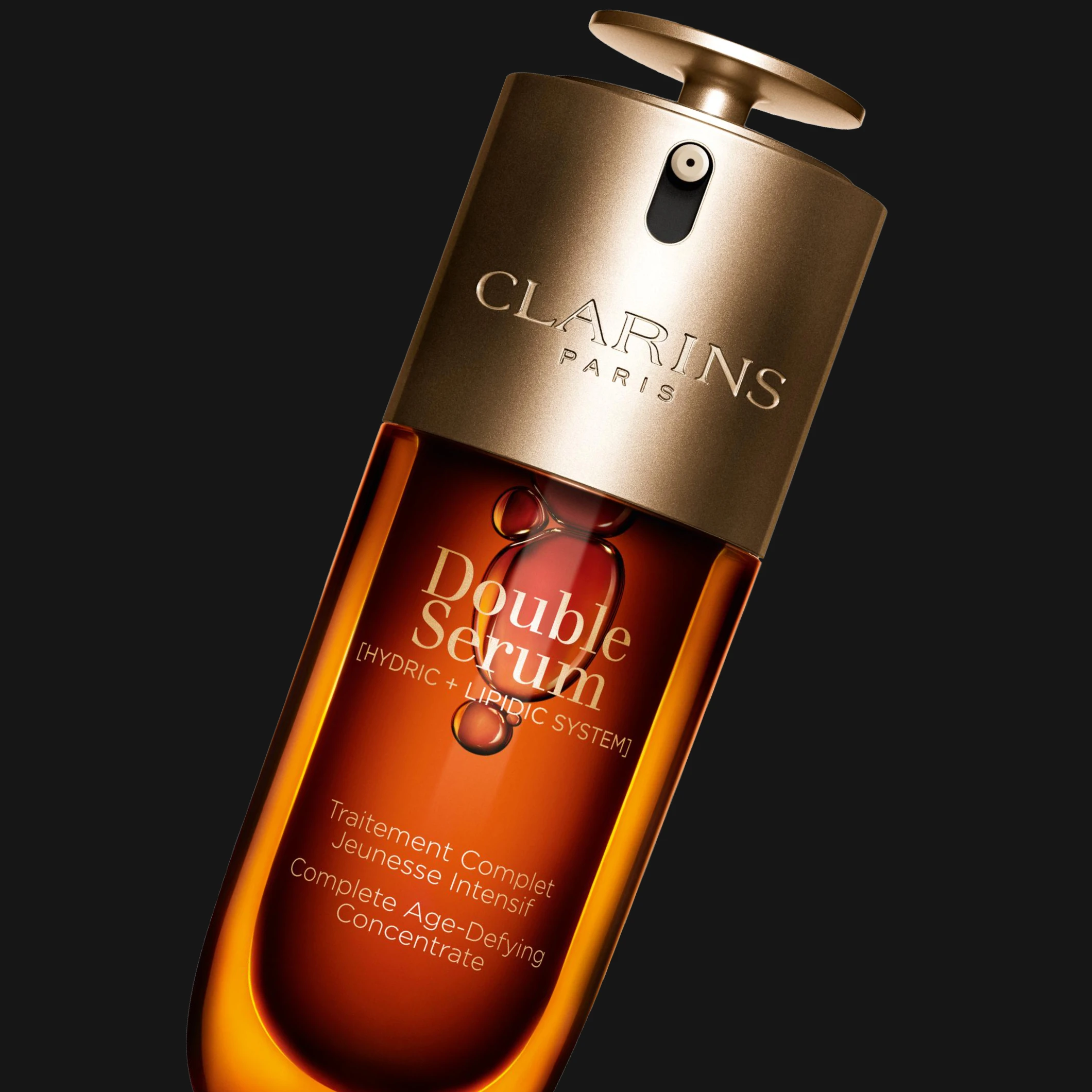 Clarins Double Serum hudvårdsserum i brun och guldfärgad pumpflaska mot svart bakgrund. Synlig text inkluderar “CLARINS PARIS”, “Double Serum”, “[HYDRIC + LIPIDIC SYSTEM]” och “Complete Age-Defying Concentrate”.