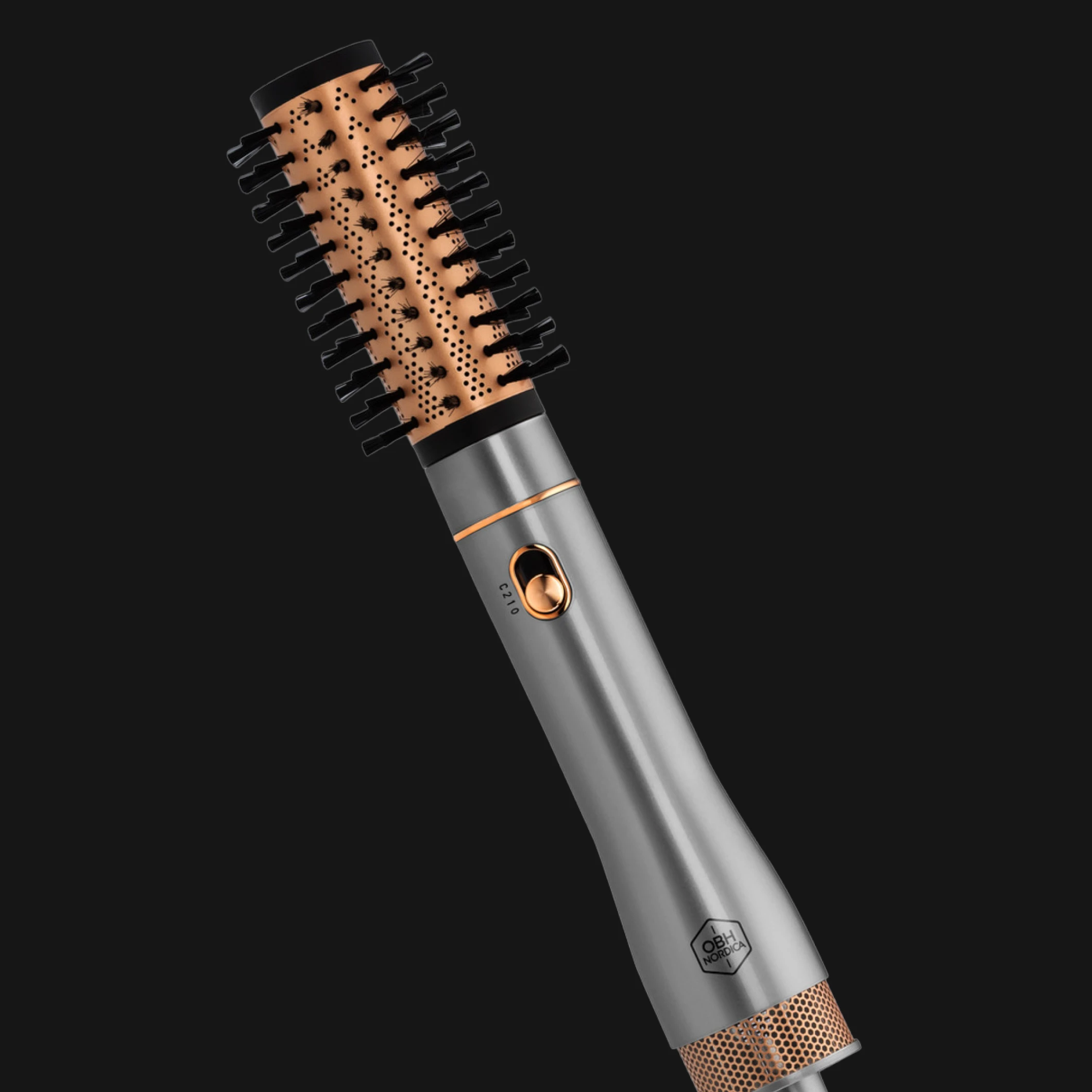 Rund värmeborste för hårstyling från OBH Nordica med metallgrå handtag, kopparfärgad borstcylinder och svarta borst mot svart bakgrund. Handtaget visar en knapp och texten “OBH Nordica”.