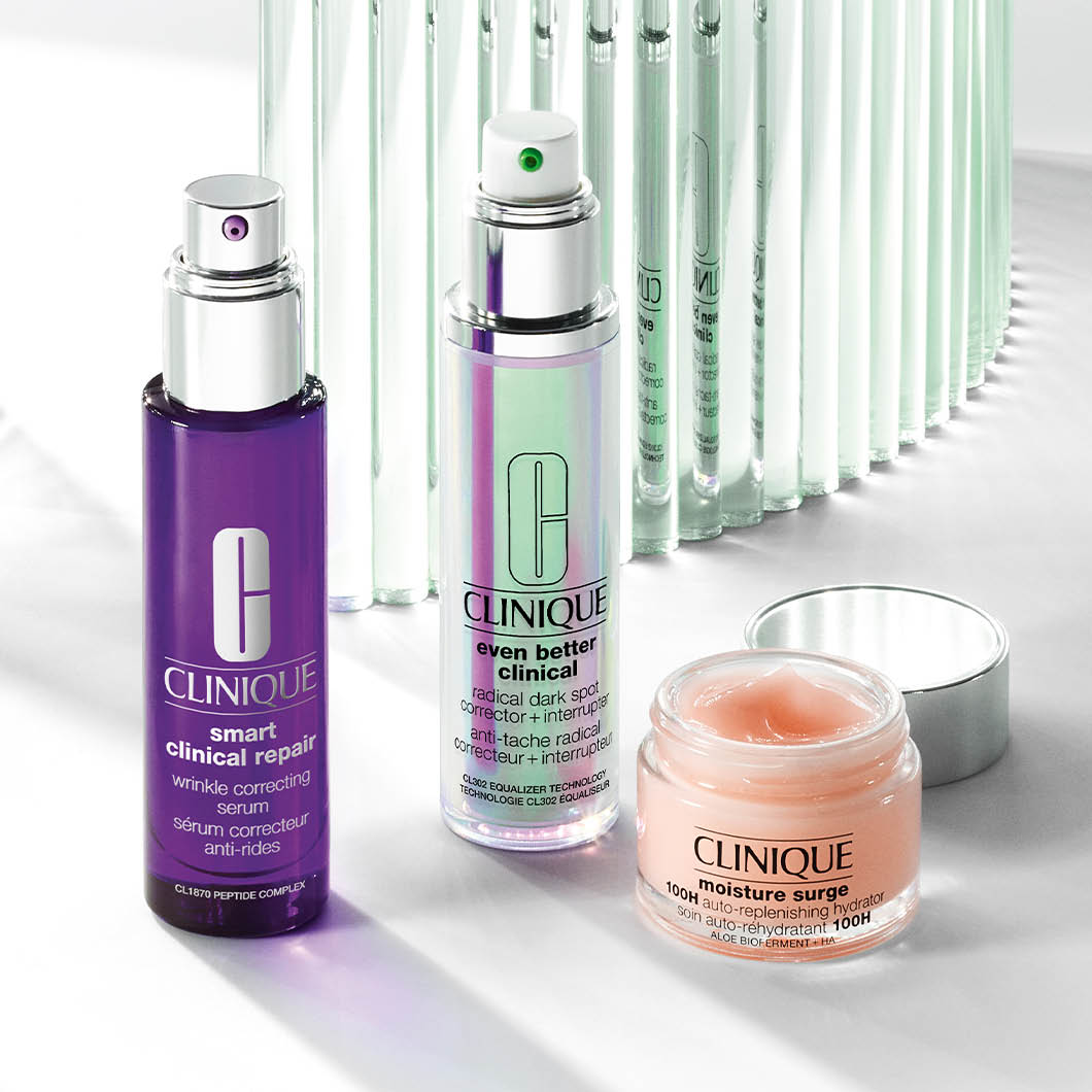 Tre hudvårdsprodukter från Clinique står framför en spegelliknande bakgrund: “Smart Clinical Repair Wrinkle Correcting Serum”, “Even Better Clinical Radical Dark Spot Corrector + Interrupter” och “Moisture Surge 100H Auto-Replenishing Hydrator”. En burk med gelkräm är öppen.
